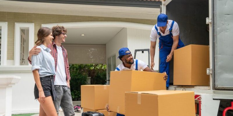 two-men-movers-blue-uniform-lift-cardboard-box-unloading-from-truck-moving-house-service_34755-1524